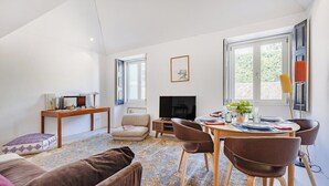 A living room with a sofa, a coffee table, a TV, a fireplace, and a dining area with chairs and a table. - Rosarinho Cruz invites to her Atelier by the Sea (Porto)