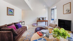 A modern living room with a brown sofa, a dining table set with plates and glasses, a TV, and a patterned rug. - Rosarinho Cruz invites to her Atelier by the Sea (Porto)