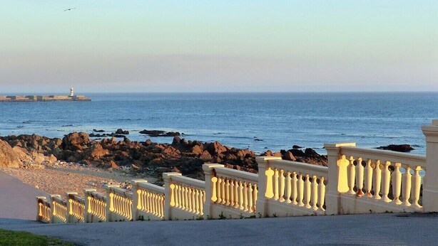A coastal walkway with a railing, a rocky shoreline, and a distant lighthouse. - Rosarinho Cruz invites to her Atelier by the Sea (Porto)