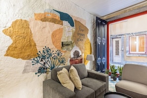 Ein gemütlicher Wohnbereich mit einer Couch, einem Wandbild und Blick auf die Straße.