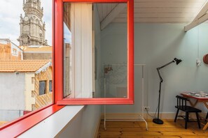 Ein Zimmer mit einem großen Fenster, einem Schreibtisch mit Stuhl, einer Stehlampe und einer Heizung.