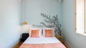 Un dormitorio con cama, almohadas, mesita de noche, lámpara y un adorno en la pared.