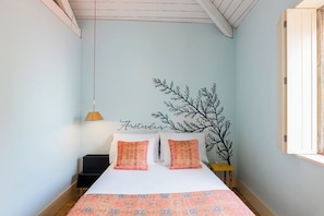 Ein Schlafzimmer mit einem Bett, Kissen, einem Nachttisch, einer Lampe und einer Wanddekoration.