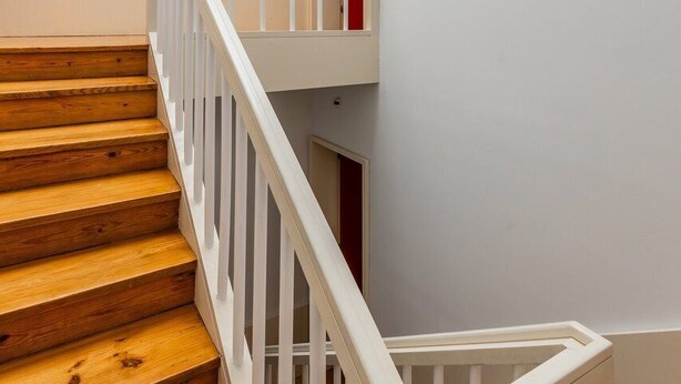 Una escalera de madera con barandillas blancas que lleva a un rellano con una puerta roja.