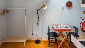 Una habitación con techo inclinado, una mesa con sillas, una lámpara de pie y un perchero.