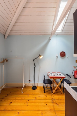 Ein Zimmer mit schrägen Wänden, einem Tisch mit Stühlen, einer Stehlampe und einem Kleiderständer.