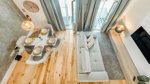Ein modernes Wohnzimmer mit einer Couch, einem Esstisch gedeckt mit Tellern und einem großen Fenster mit Vorhängen.