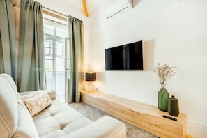 A living room with a sofa, a flat-screen TV mounted on the wall, a wooden console table, and a vase with dried flowers. - Santa Catarina Charming Loft (Porto)