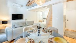 Ein modernes Interieur mit Essbereich, einer Couch, einem Fernseher und einer Decke mit freiliegenden Balken.