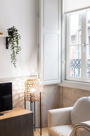 Ein Zimmer mit Fernseher, Pflanze, Lampe und Fenster mit Blick auf Gebäude.