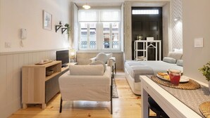 Ein gemütliches Hotelzimmer mit einer Couch, einem kleinen Tisch mit einem Getränk, einem Fernseher, einem Fenster mit Aussicht und einer Tür, die auf einen Balkon führt.