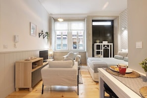 Ein gemütliches Hotelzimmer mit einer Couch, einem kleinen Tisch mit einem Getränk, einem Fernseher, einem Fenster mit Aussicht und einer Tür, die auf einen Balkon führt.