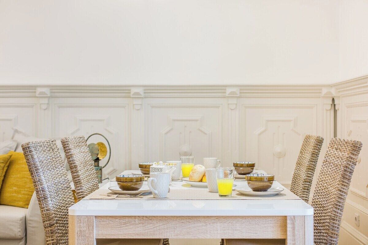 A dining table set with breakfast items, surrounded by wicker chairs, in a room with white walls and a white ceiling.