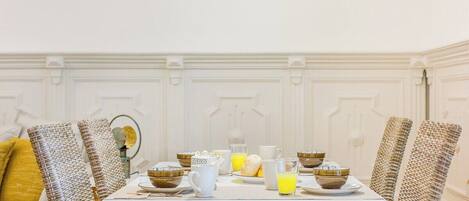 A dining table set with breakfast items, surrounded by wicker chairs, in a room with white walls and a white ceiling.