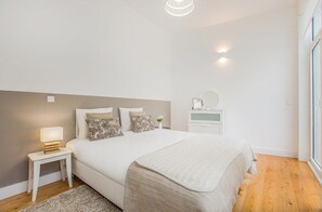 Ein Schlafzimmer mit Bett, Nachttisch, Lampe und einer kleinen weißen Kommode.
