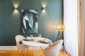 Ein Essbereich mit einem runden Tisch, zwei weißen Stühlen, einer Wandleuchte und einer Stehlampe.