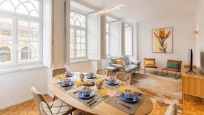 A dining area with a round table set for four, a sofa, and a television on a wooden stand. - São Bento Deluxe 42 with Balcony (Porto)