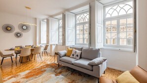 A modern living room with a sofa, dining table, chairs, and large windows. - São Bento Deluxe 42 with Balcony (Porto)