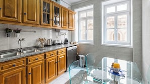 A kitchen with wooden cabinets, a stainless steel sink, and a glass dining table with a bowl of fruit. - São Bento Deluxe 42 with Balcony (Porto)