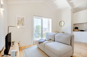 Ein modernes Wohnzimmer mit einer Couch, einem Flachbildfernseher, einem Essbereich mit Tisch und Stühlen sowie einem großen Fenster mit Aussicht.
