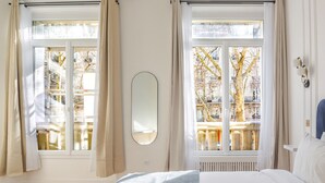 Un dormitorio con una cama grande, dos ventanas con cortinas, un radiador y un espejo montado en la pared.