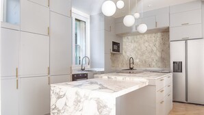 Una cocina moderna con encimeras de mármol, armarios blancos y tiradores dorados.