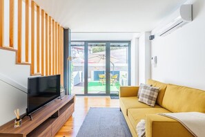Ein modernes Wohnzimmer mit einem Fernseher auf einem Holzschrank, einem gelben Sofa und einer Glastür zum Außenbereich.