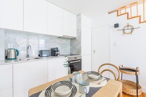 Eine kompakte Küche mit weißen Schränken, einer Marmor-Spritzschutzwand, einem eingebauten Backofen und einem Essbereich mit Holztisch und Stühlen.
