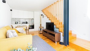 Ett modernt vardagsrum med en soffa, TV, en trappa i trä och ett köksområde.