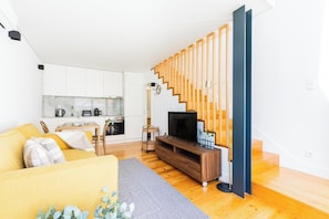 Ein modernes Wohnzimmer mit Sofa, Fernseher, einer Holztreppe und einer Küchenzeile.