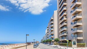 Eine Küstenstraße mit modernen Wohngebäuden, blauem Himmel und einem Strand im Hintergrund.