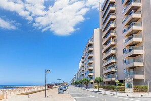 Eine Küstenstraße mit modernen Wohngebäuden, blauem Himmel und einem Strand im Hintergrund.