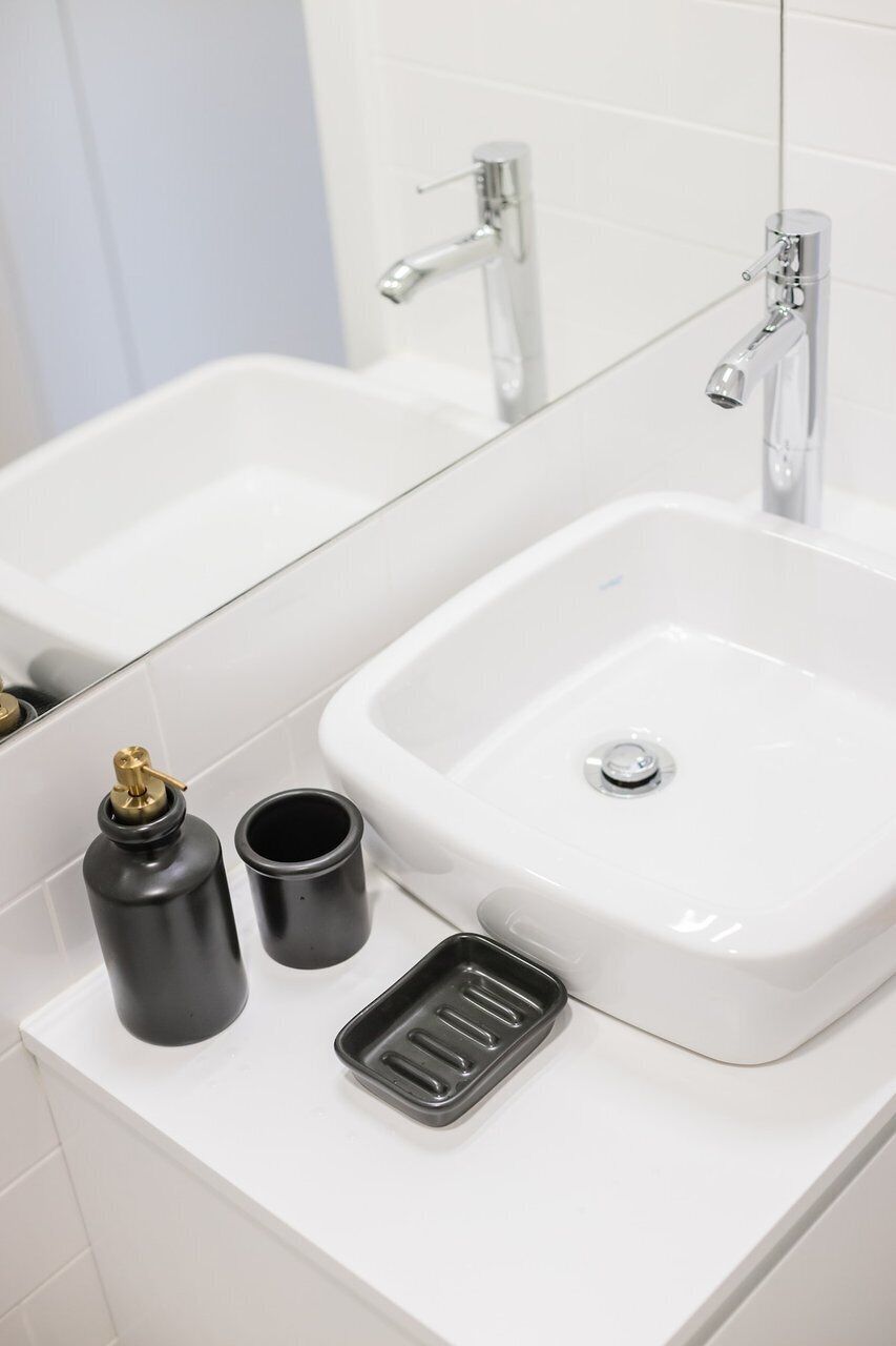 Ein Badezimmer mit einem weißen Waschbecken, einem Spiegel und zwei schwarzen Behältern auf der Ablagefläche.