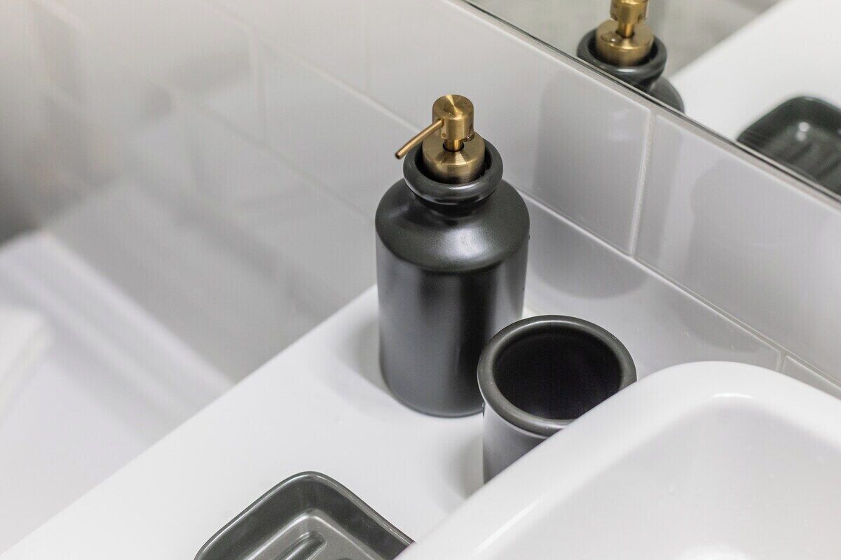 A bathroom with a white sink, a black soap dispenser, and a mirror reflecting a faucet.