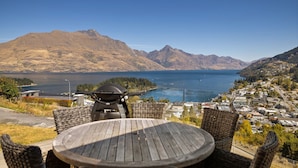 Una terrazza con un tavolo e sedie rotonde che si affaccia su un lago e montagne.