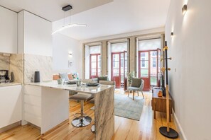 A modern kitchen with a marble island, wooden flooring, and large windows with red frames. - Sol Downtown Studio with Juliet Balcony (Porto)