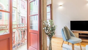 Une pièce avec une grande fenêtre, un téléviseur, une chaise et un vase rempli de fleurs.