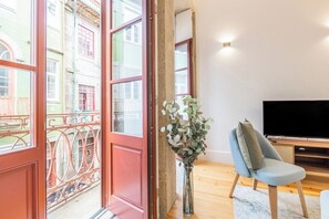 A room with a large window, a television, a chair, and a vase with flowers. - Sol Downtown Studio with Juliet Balcony (Porto)