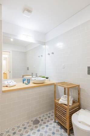 A modern bathroom with white tiles, a wooden vanity, a sink, a mirror, and a toilet. - Bonfim Perfect Stays (Porto)