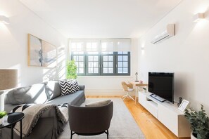A modern living room with a sofa, armchair, TV, and a small dining area. - Bonfim Perfect Stays (Porto)