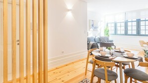 Un comedor con una mesa de madera dispuesta para cuatro personas, un sofá y una ventana con persianas.