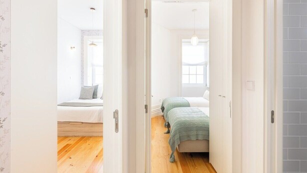 Un pasillo estrecho que conduce a un dormitorio con cama, mesita de noche y ventana.