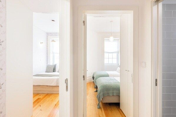 A narrow hallway leading to a bedroom with a bed, a bedside table, and a window. - Bonfim Perfect Stays (Porto)