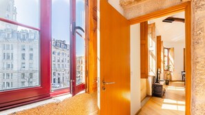A hallway with a wooden floor, a red-framed window, and a wooden door leading to another room. - Casa Fernando @ Trindade (Porto)