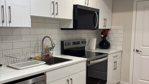 A modern kitchen with white cabinets, stainless steel appliances, and a black microwave. - Cozy Urban Hideout (Saskatoon)
