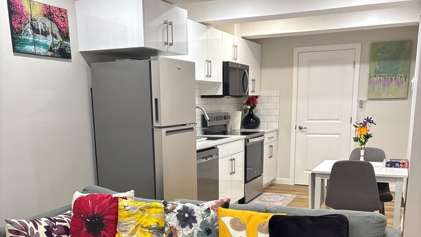 A modern living room with a grey sectional sofa, a kitchen in the background, and a dining area. - Cozy Urban Hideout (Saskatoon)