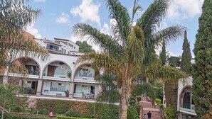 A pool area with a two-story building in the background, surrounded by palm trees and greenery. - Suite vista hermosa  (San Miguel de Allende)