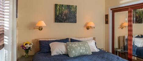 A bedroom with a large bed, two wall-mounted lamps, a painting, and a mirror.