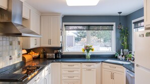 Une cuisine avec des meubles blancs, un plan de travail noir, une cuisinière et une fenêtre donnant sur l’extérieur.