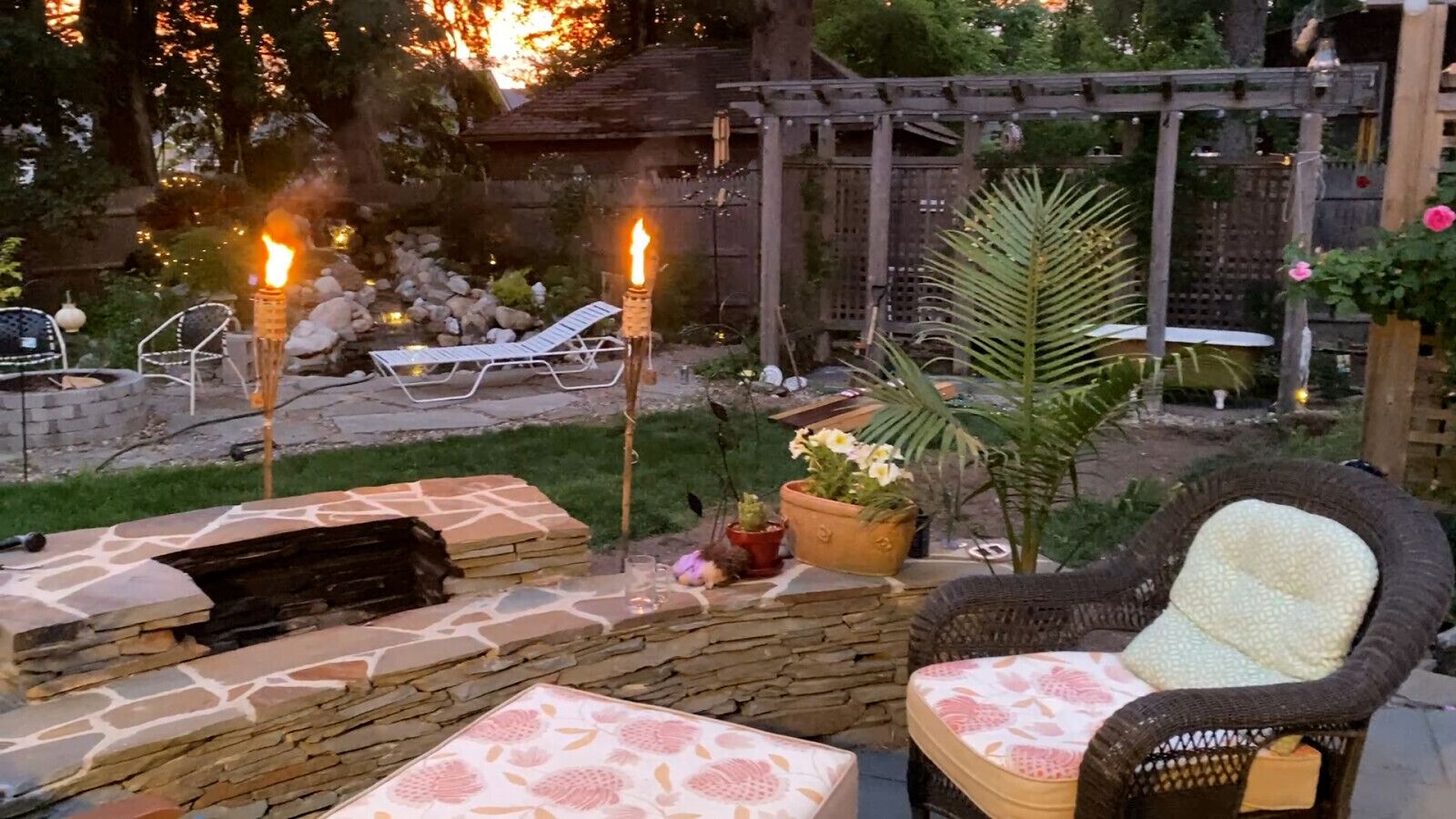 Une terrasse extérieure avec des sièges en pierre, un fauteuil en osier et un foyer agrémenté de bougies.